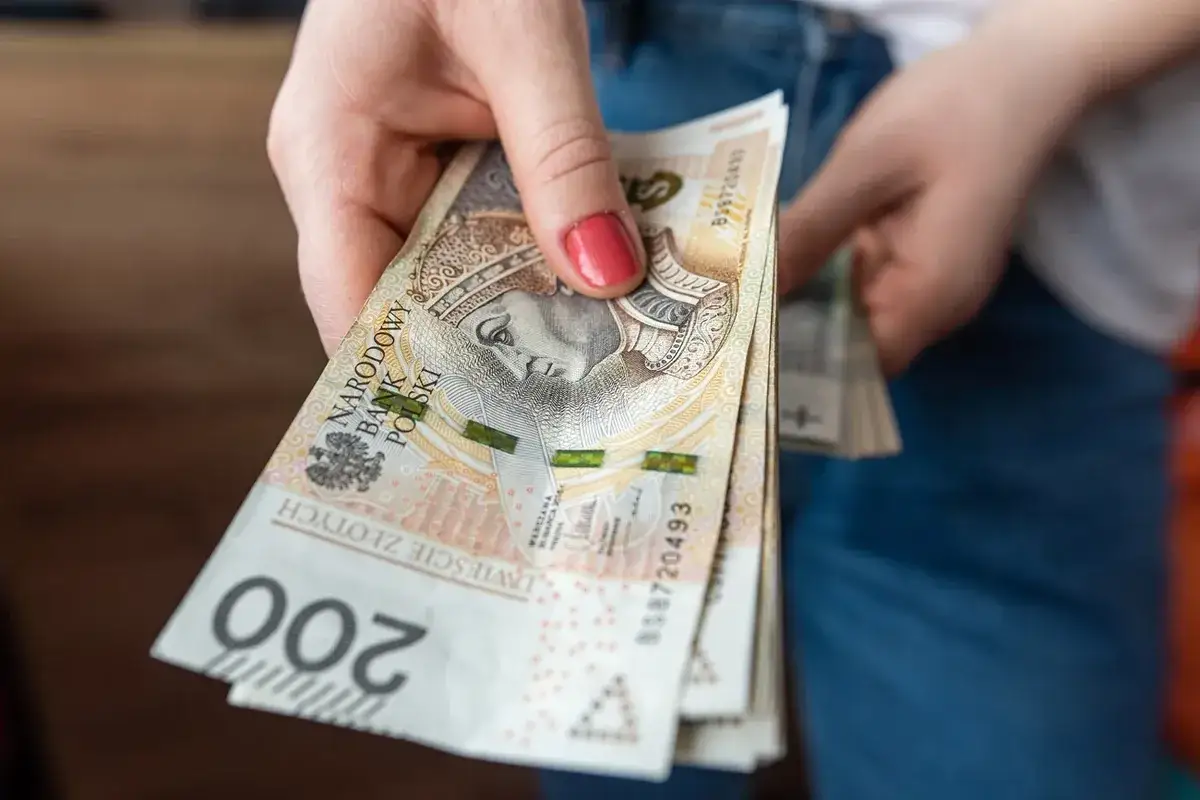 Dłoń trzyma stos banknotów 200 zł. Czy to wystarczy, by dowiedzieć się, ile wynosi najniższa emerytura netto?