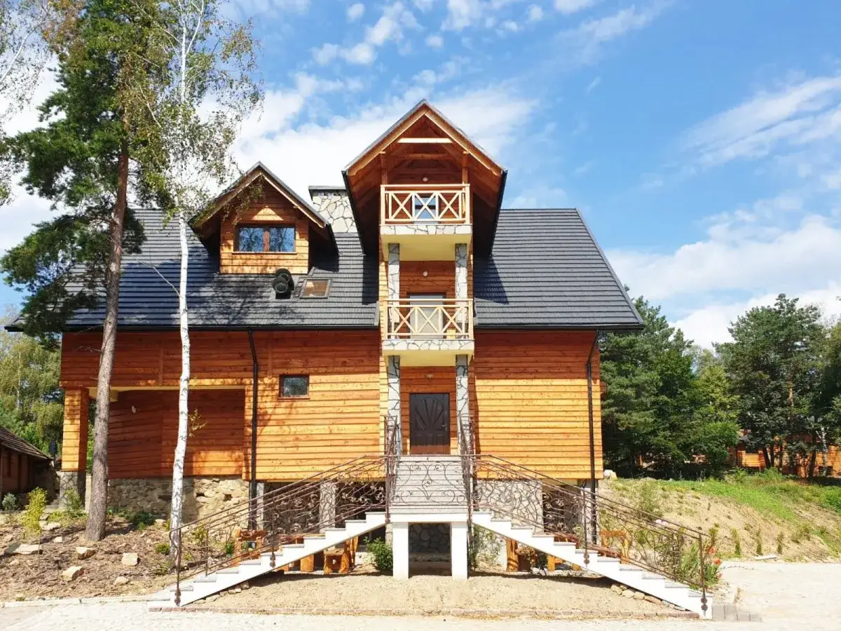 Drewniana bacówka na Jamnej z kamiennymi elementami i ozdobnymi schodami. Otoczona zielenią, zaprasza do wypoczynku.