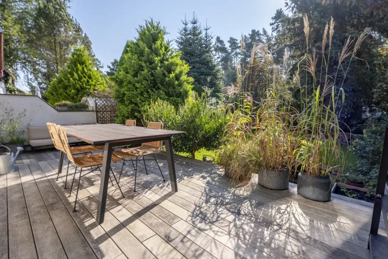 Drewniany taras z meblami i trawami ozdobnymi. Idealne miejsce, by zastanowić się, co położyć na taras, by stworzyć przytulną przestrzeń.