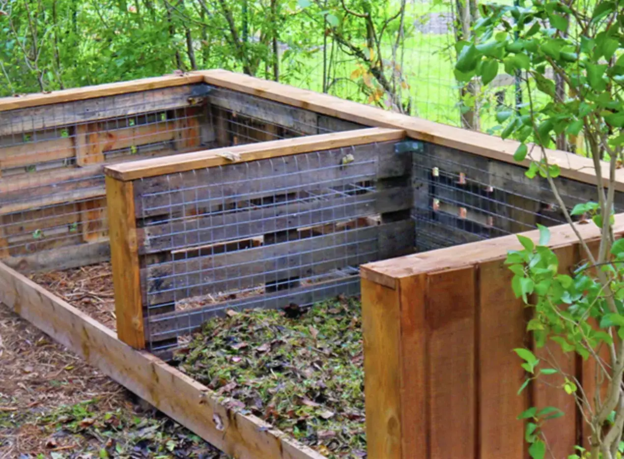 Drewniany kompostownik z siatką, bez dna, wypełniony resztkami roślin. Czy kompostownik powinien mieć dno? To pytanie, na które odpowiedź znajdziesz w praktyce.