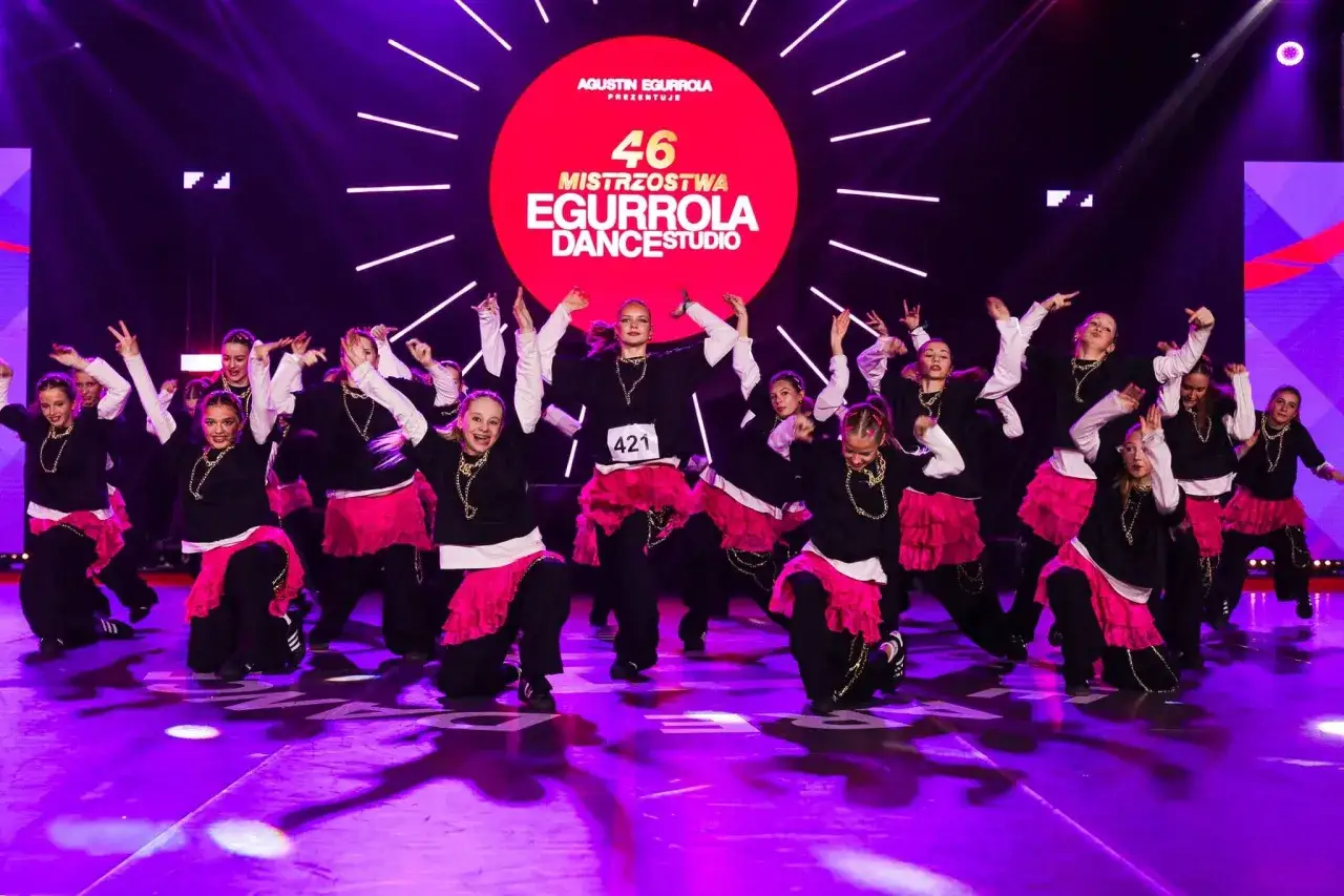 Grupa młodych tancerzy wykonuje energiczne piosenki z układem tanecznym na scenie.