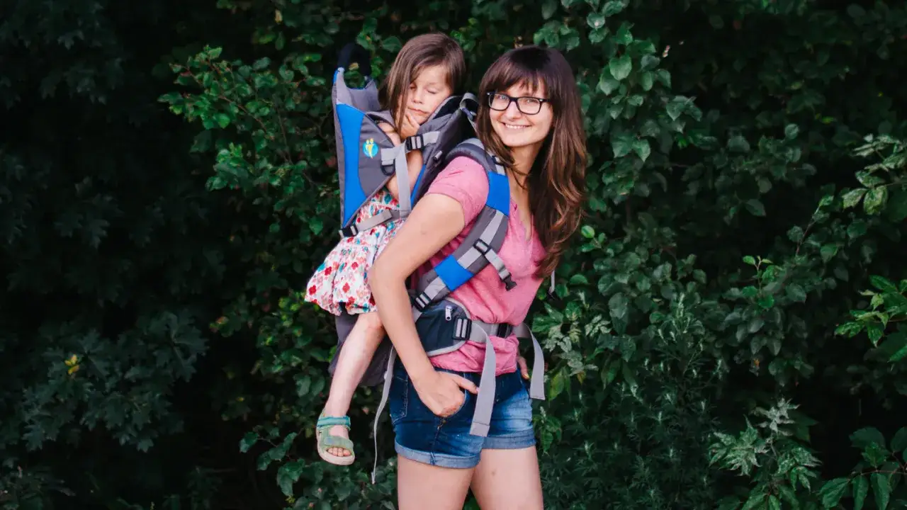 Uśmiechnięta mama z c&oacute;rką w nosidle, gotowe na wyprawę gdzie w g&oacute;ry z dziećmi.