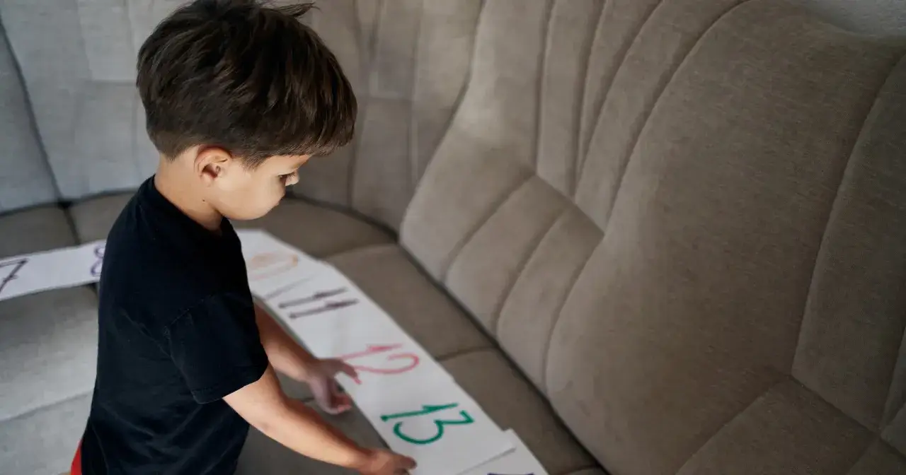 Chłopiec ze spektrum autyzmu układa karty z liczbami na kanapie. Skupiony na nauce, odkrywa świat liczb.