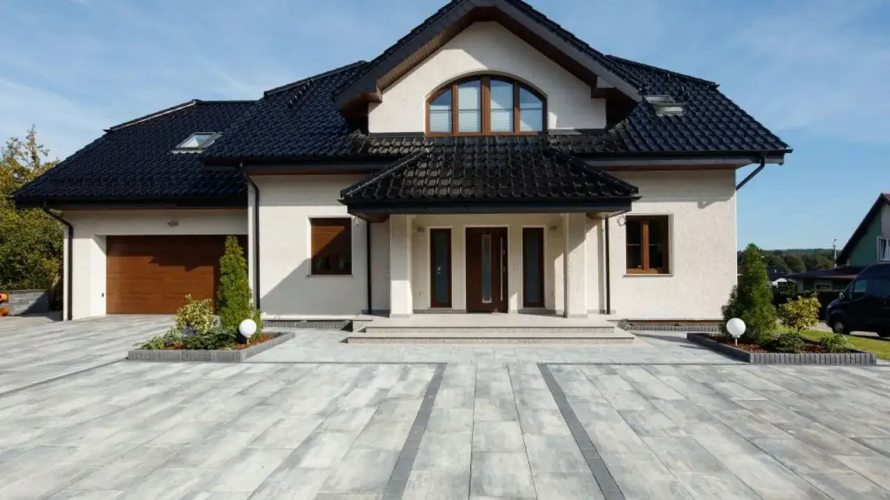 Nowoczesny dom z garażem i wejściem, przed którym rozciąga się elegancki podjazd z płyt betonowych.