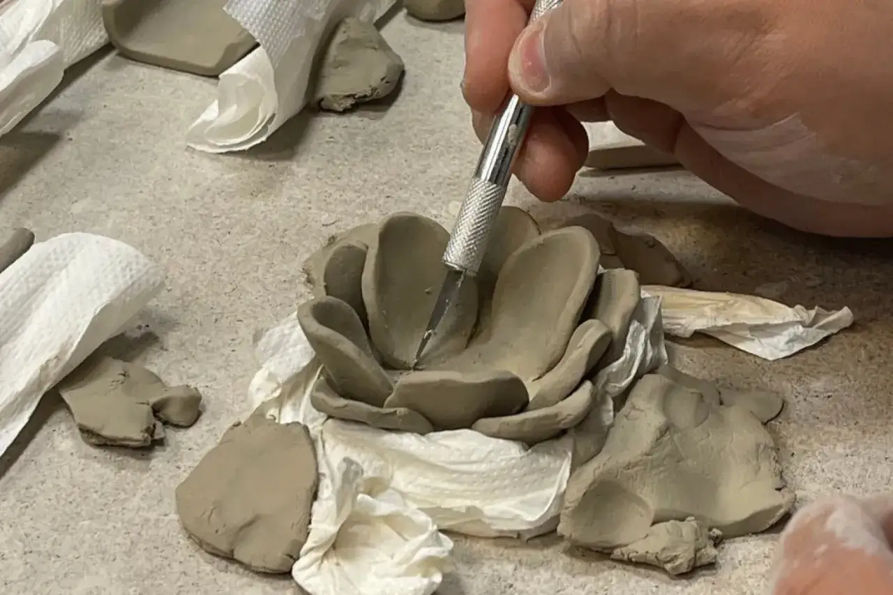 Podczas zajęć z ceramiki powstaje gliniana r&oacute;ża. Dłoń z narzędziem precyzyjnie modeluje płatki.