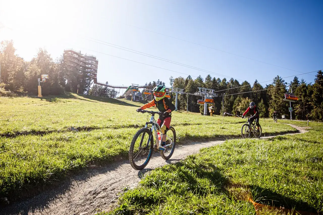 Dzieci zjeżdżają na rowerach po trasie w jednym z najlepszych bike parków w Polsce. W tle widoczna wieża widokowa i kolejka krzesełkowa.