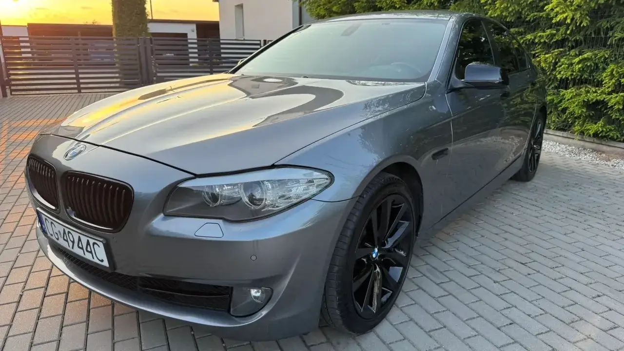 Eleganckie bmw f10 w kolorze szarym, z czarnymi felgami, zaparkowane na podjeździe z kostki brukowej.