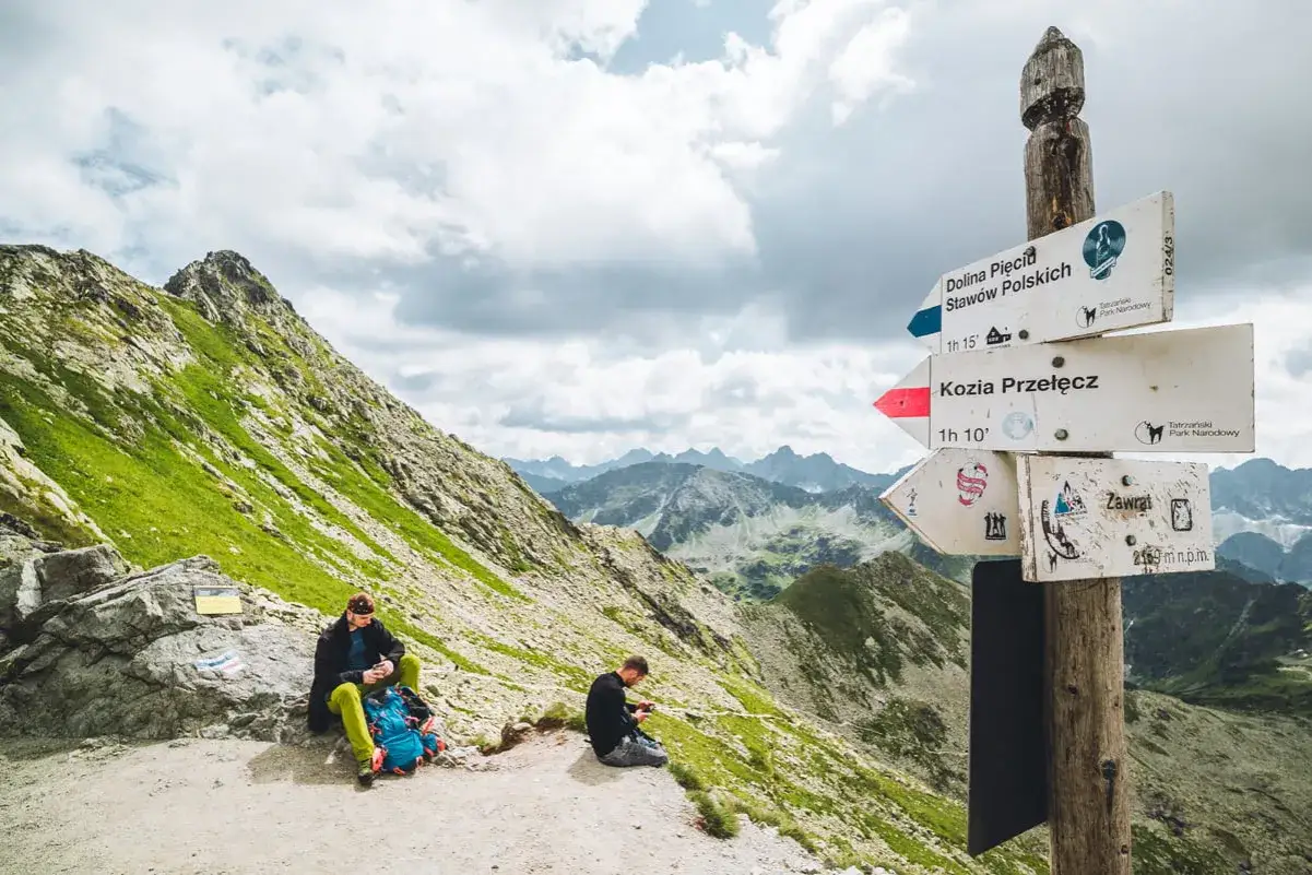 Na szlaku do Doliny Pięciu Staw&oacute;w Polskich, przy znaku na Kozią Przełęcz, odpoczywają turyści.