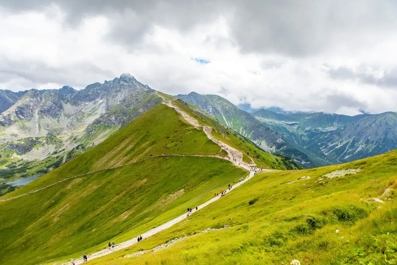 Tłumy turystów na szlaku w Tatrach. Piękny dzień na hiking po polsku, z widokiem na zielone zbocza i skaliste szczyty.
