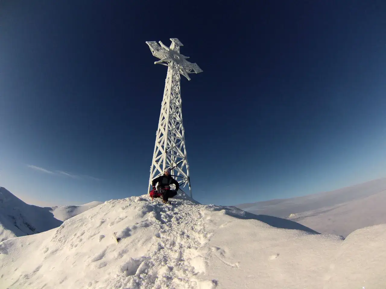 Ośnieżony Kościelec zimą. Turysta w kasku i z plecakiem przycupnął na szczycie, podziwiając mroźny krajobraz.