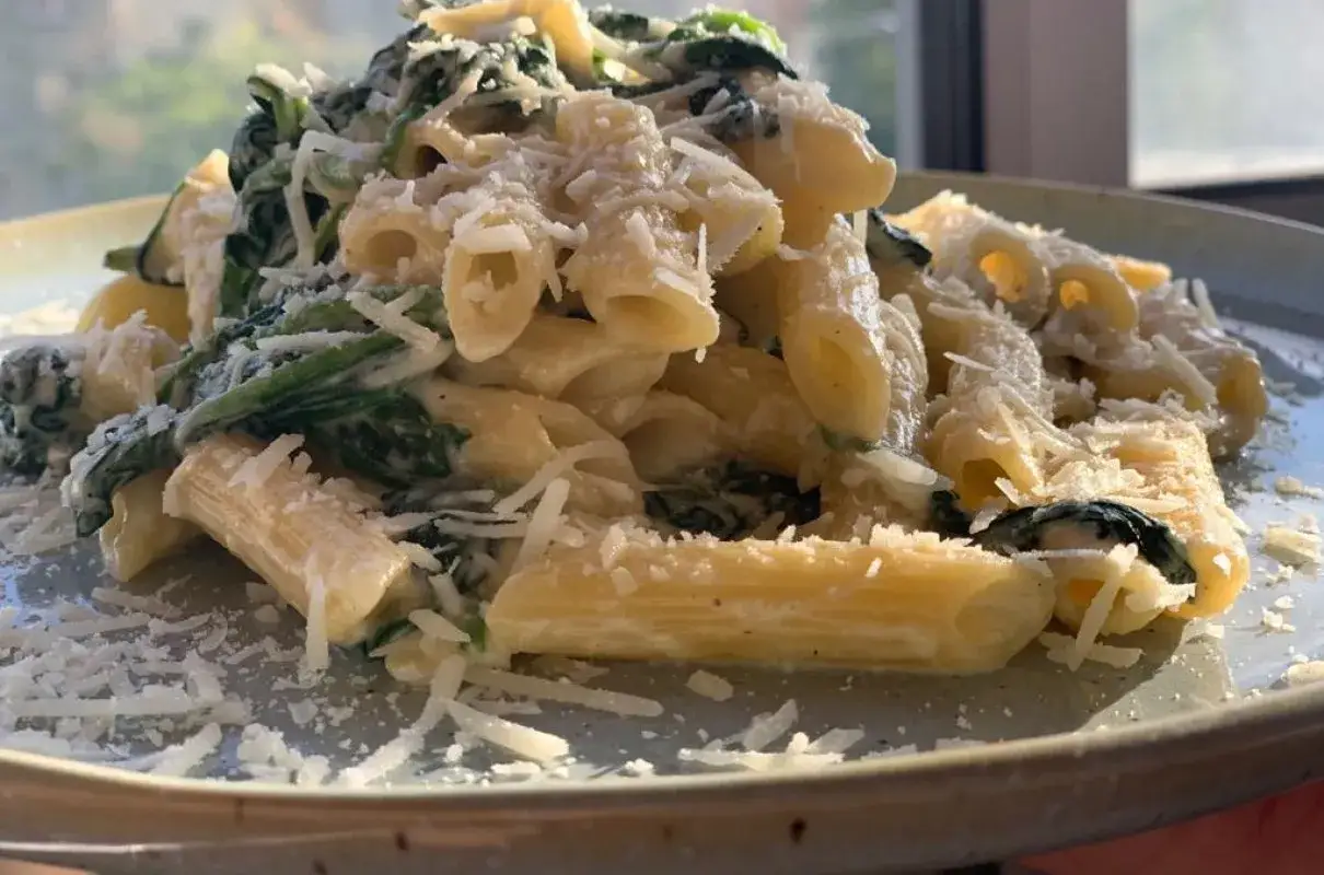 Penne z kremowym sosem i świeżym szpinakiem, posypane tartym parmezanem. Pyszny szpinak z makaronem na talerzu.