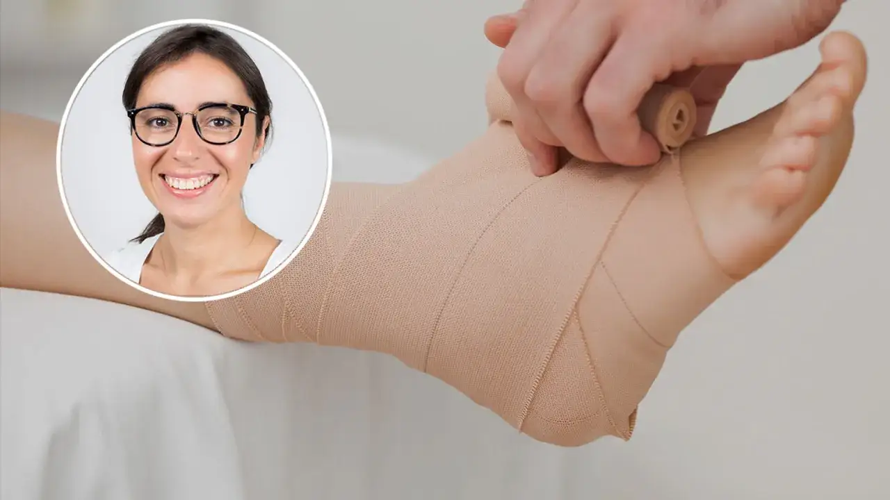 Uśmiechnięta kobieta w okularach patrzy na nogę z bandażem. Objawy skręconego stawu skokowego mogą być łagodzone przez odpowiednie opatrzenie.