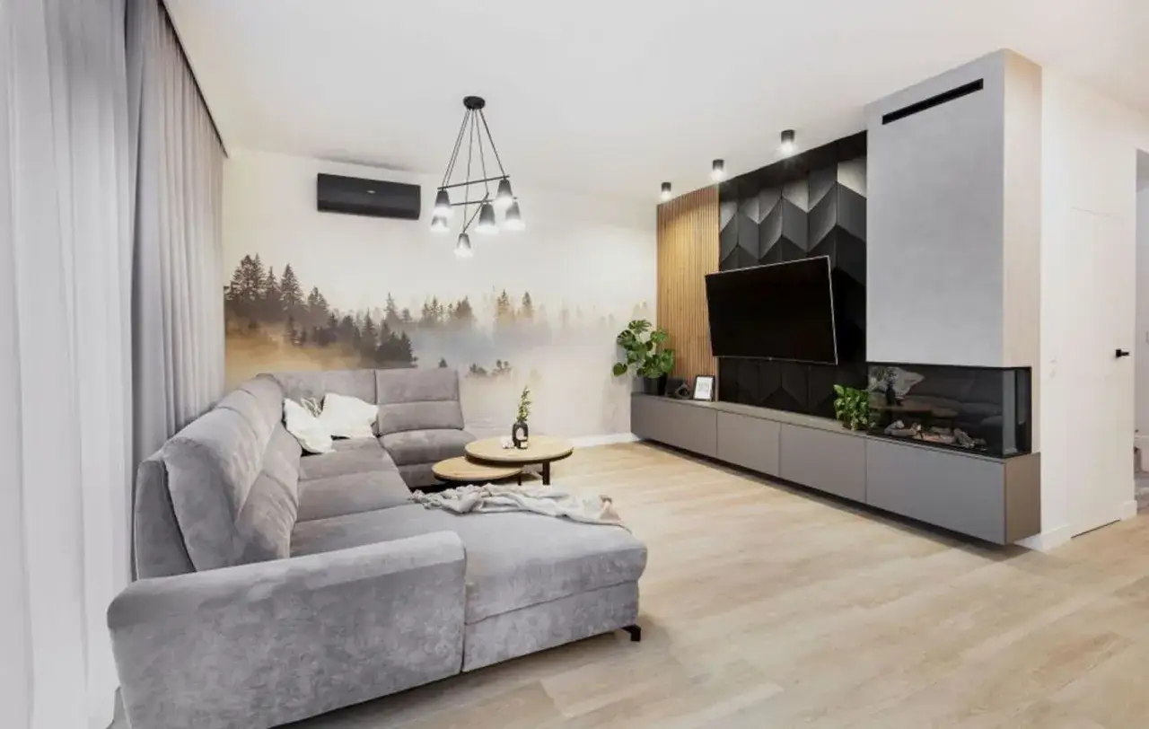 Nowoczesny salon z szarą sofą, tapetą z lasem i kominkiem. Zastanawiasz się, jaka moc żarówki led do salonu?