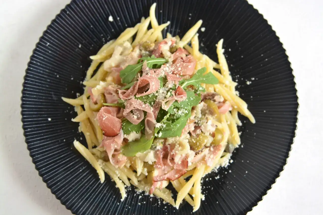 Pyszny makaron z szynką parmeńską, rukolą i parmezanem na czarnym talerzu.