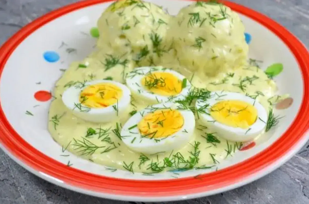 Pyszne jajka w sosie koperkowym, idealne co na obiad z jajek. Podane na talerzu z kolorowymi kropkami.