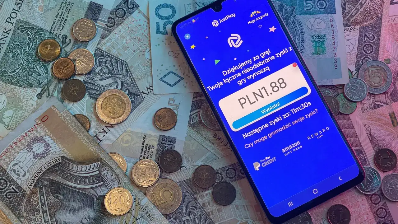 Na jakich aplikacjach można zarobić? Smartfon z aplikacją JustPlay pokazuje zarobione PLN 1.88 na tle polskich banknot&oacute;w i monet.