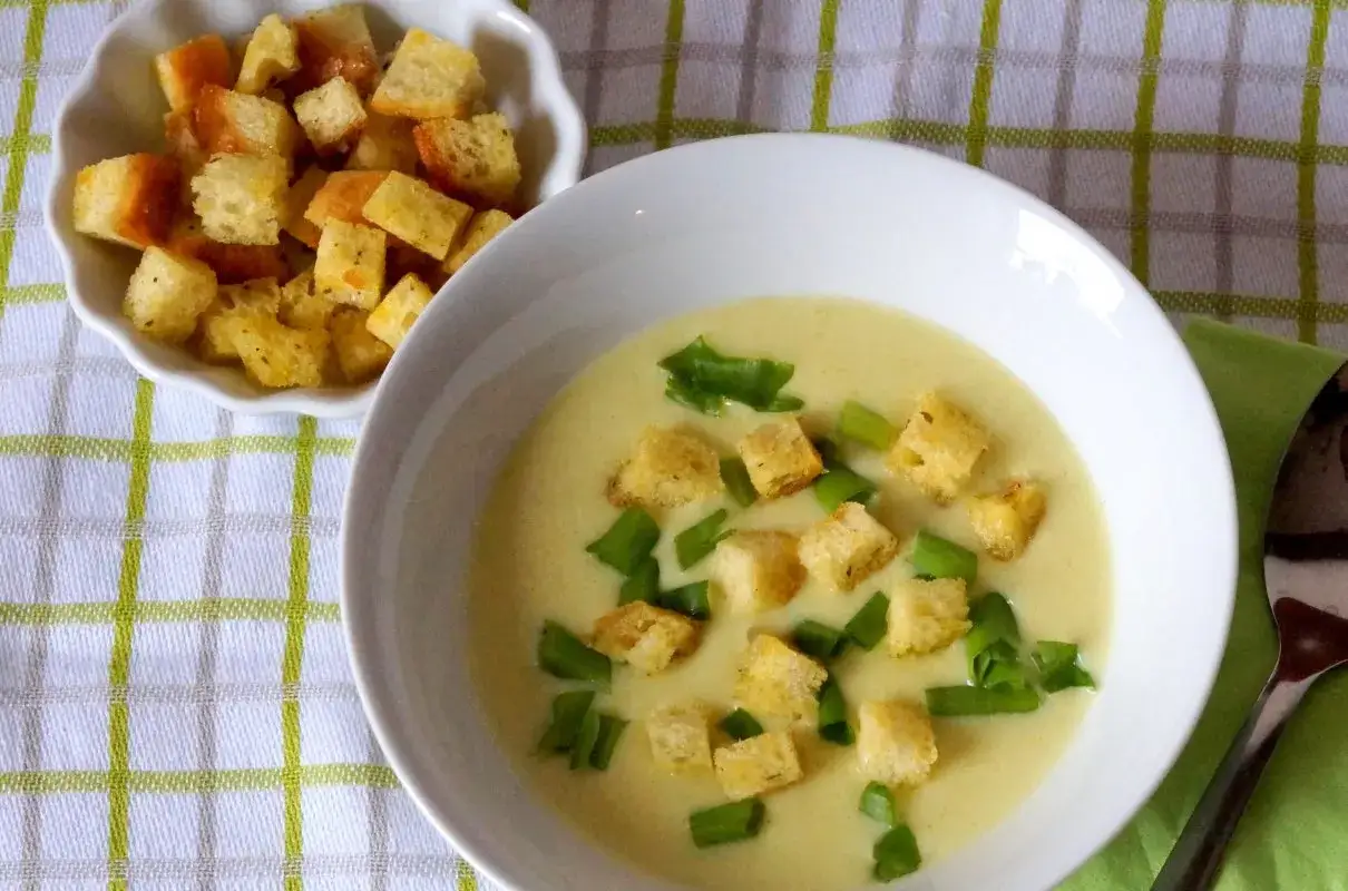 Kremowa zupa z porów, udekorowana grzankami i szczypiorkiem, podana z miseczką chrupiących grzanek.