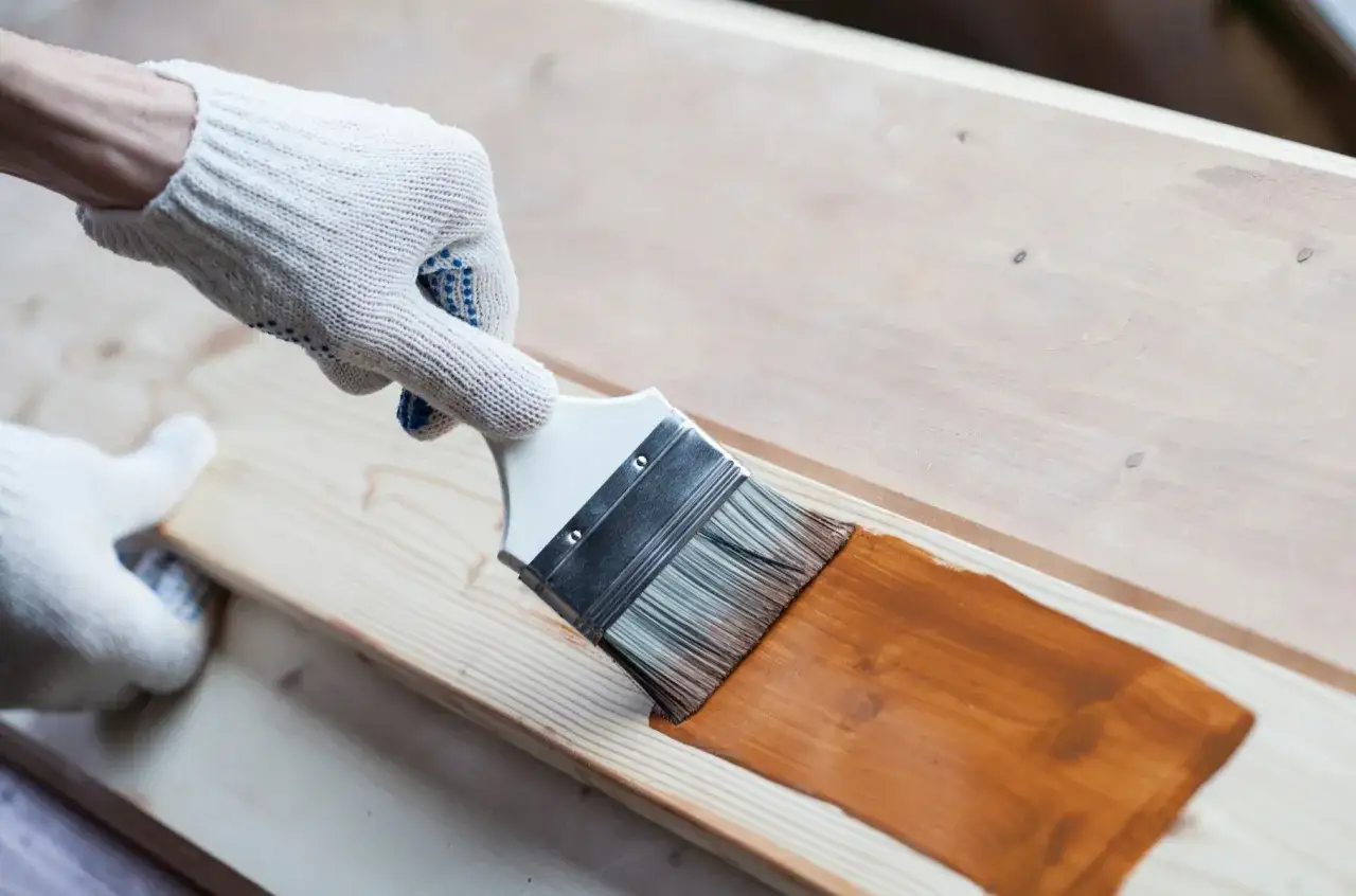 Rękawiczki ochronne i pędzel pomagają w procesie jak przygotować drewno do malowania. Brązowa bejca nadaje mu nowy wygląd.