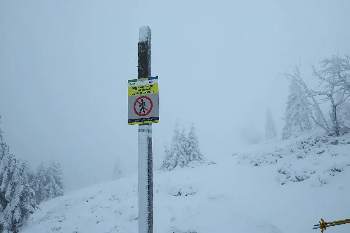 Znak informuje, że szlaki w Karkonoszach są zamknięte. Widać go na tle zaśnieżonego, mglistego krajobrazu.