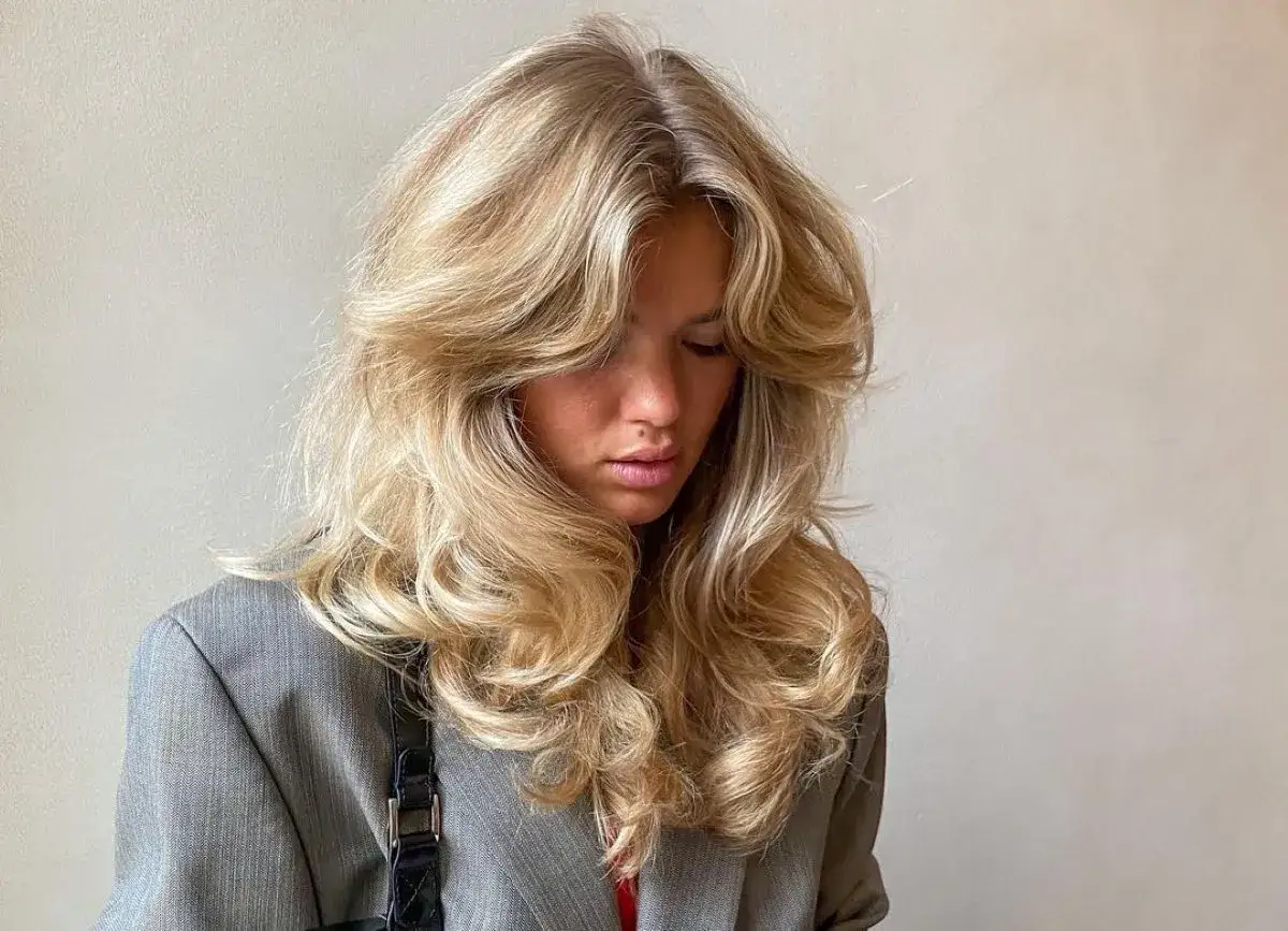 Grzywki do okrągłej twarzy: ta fryzura z burzą blond loków i grzywką na bok idealnie podkreśla rysy.