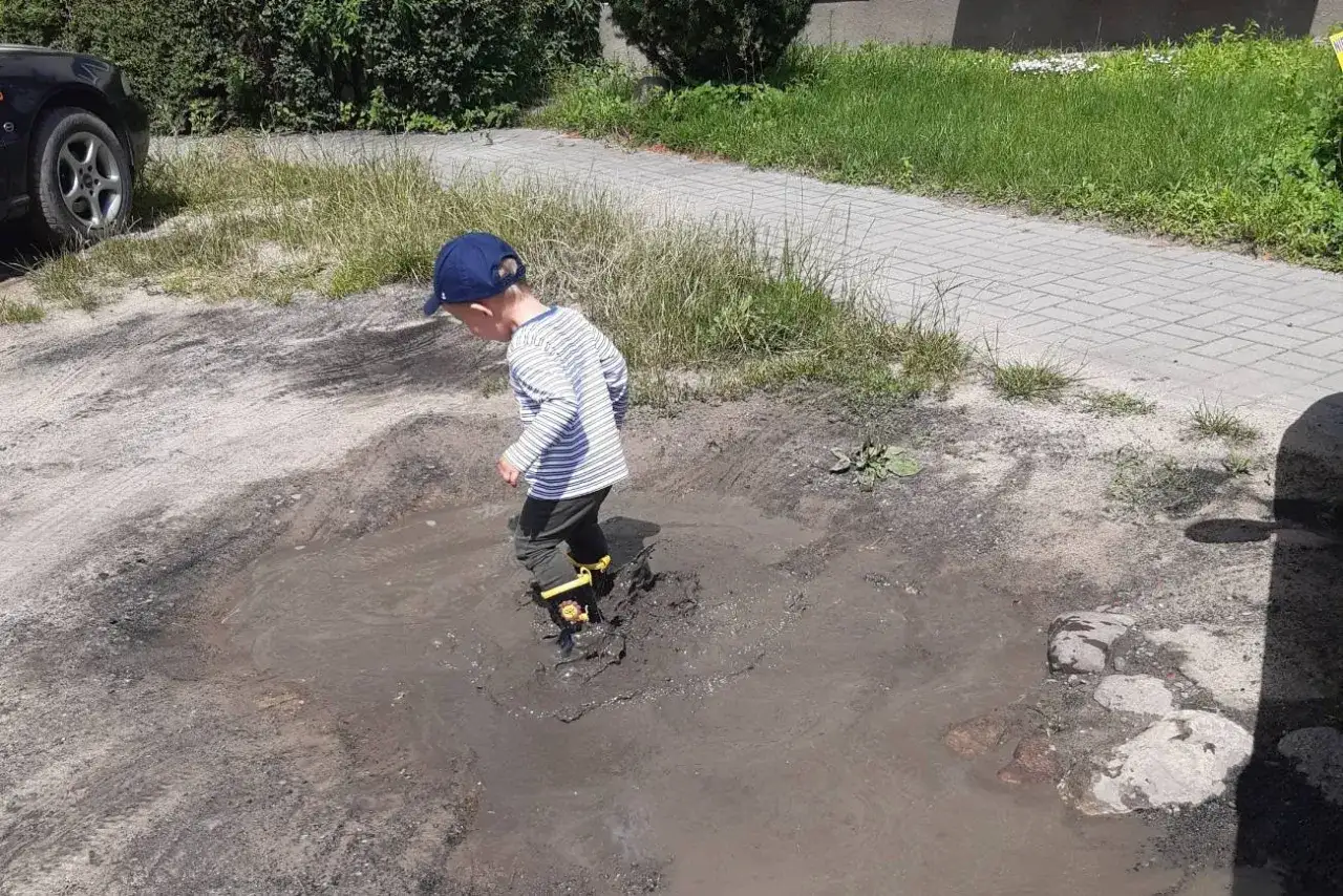 Chłopiec w kaloszach bryzga w kałuży, ćwicząc kr&oacute;tkie łamańce językowe dla dzieci.