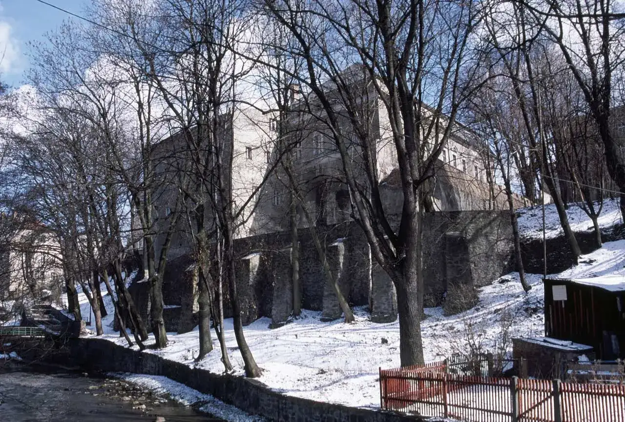 Zimowy widok na Nową Rudę zamek, otoczony nagimi drzewami i ośnieżonymi zboczami.