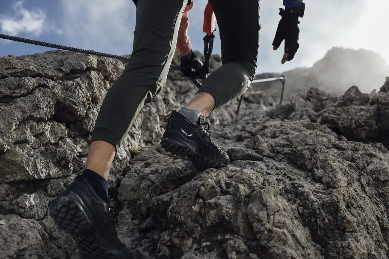 Osoba wspina się po skalistej ścieżce w butach podejściowych, kt&oacute;re zapewniają pewność kroku.