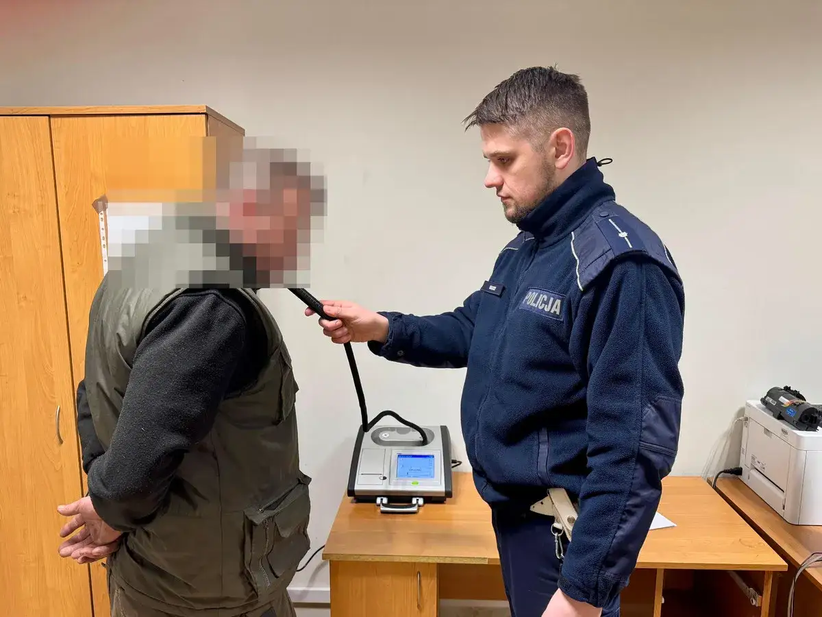 Policjant bada kierowcę alkomatem. Grozi mu mandat za brak prawa jazdy.