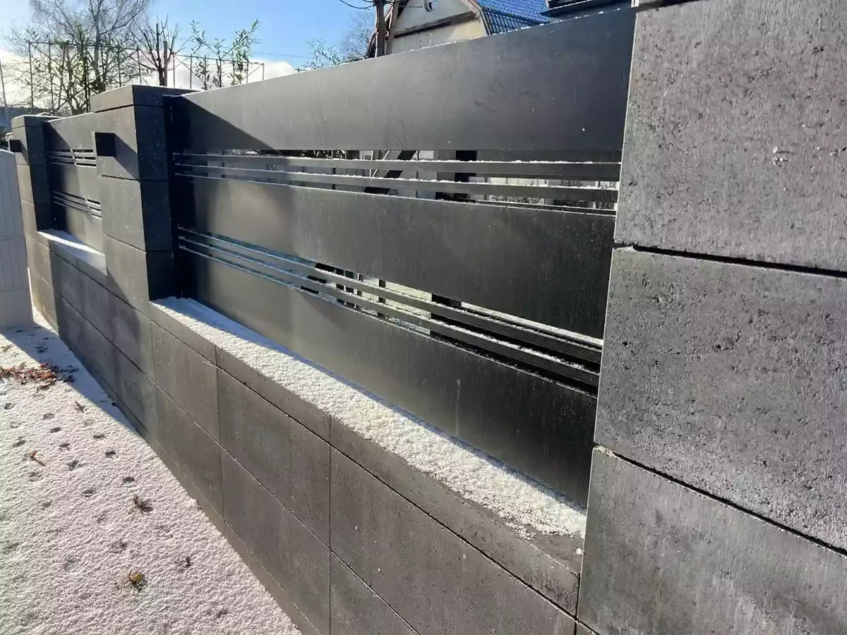 Nowoczesne ogrodzenie murowane pełne z czarnego kamienia, z metalowymi wstawkami, pokryte lekkim szronem.