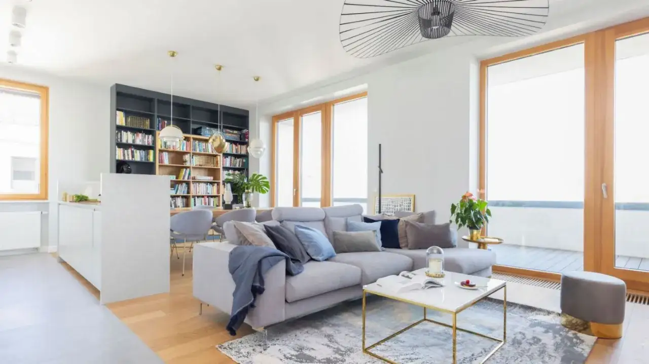 Przytulny salon w drewnie i bieli, z szarą sofą, białym stolikiem kawowym i regałem pełnym książek.