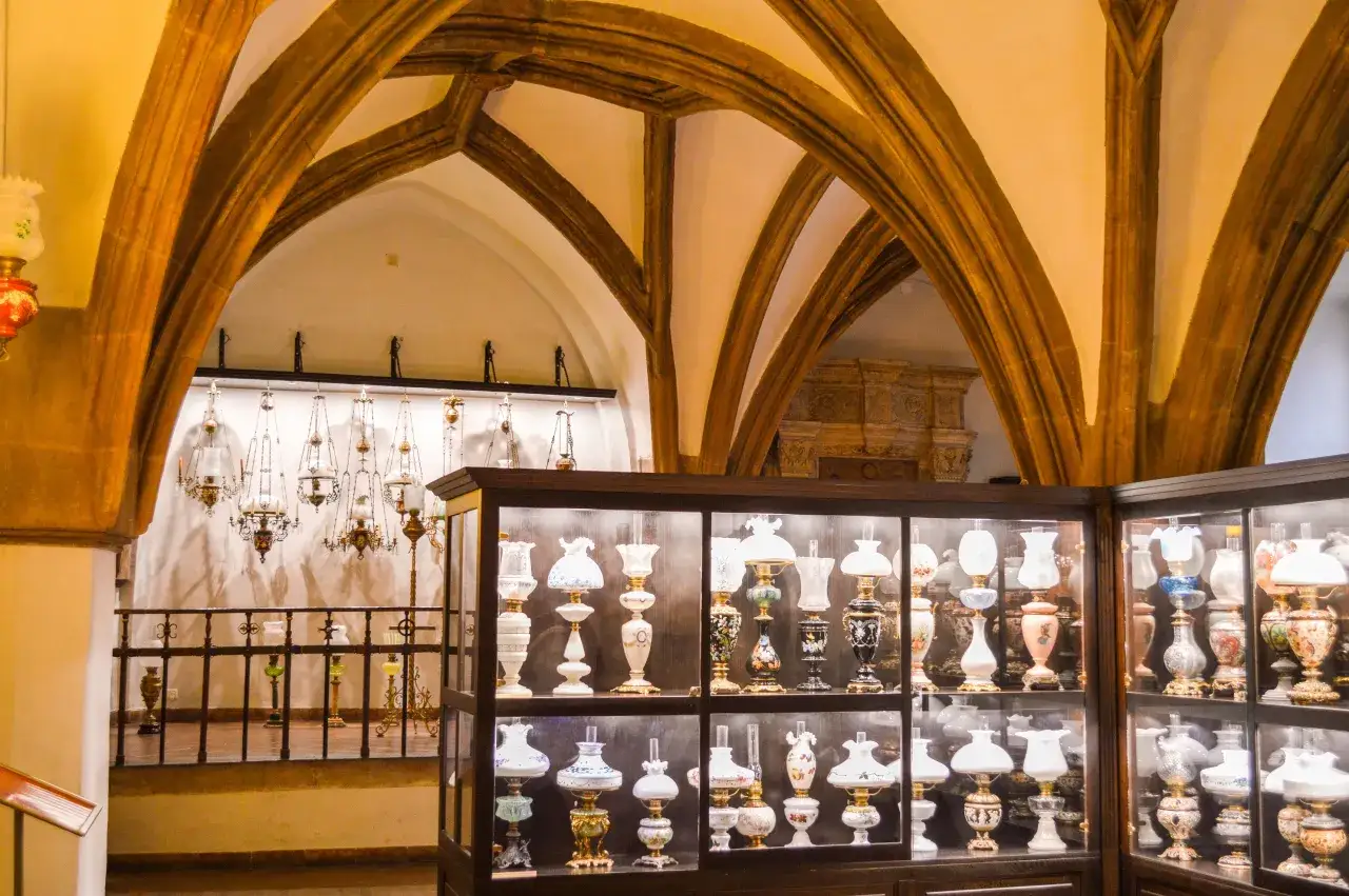 Wnętrze muzeum sztuki mieszczańskiej Wrocław. W gablotach zabytkowe lampy naftowe i świeczniki.