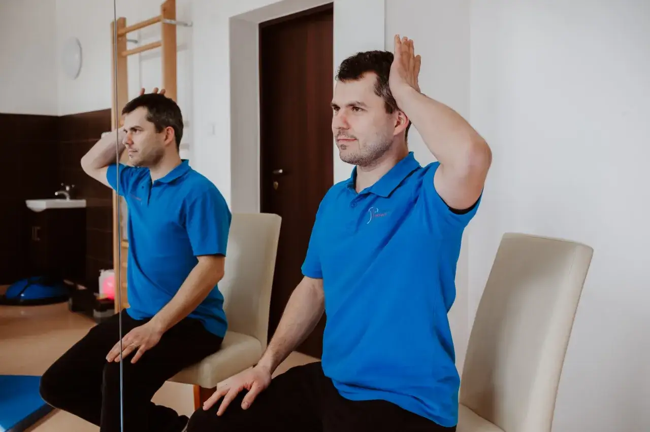 Mężczyzna w niebieskiej koszulce wykonuje ćwiczenie na szyję, opierając dłoń o głowę. To może być jeden z domowych sposobów na kręcz szyi.