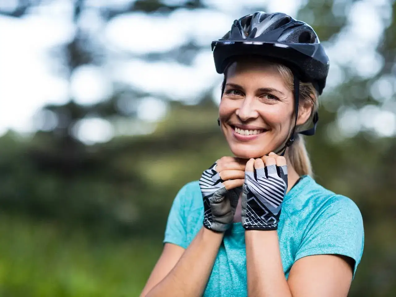 Uśmiechnięta rowerzystka zapina kask. Dowiedz się, jak zmierzyć głowę do kasku, by zapewnić sobie bezpieczeństwo.