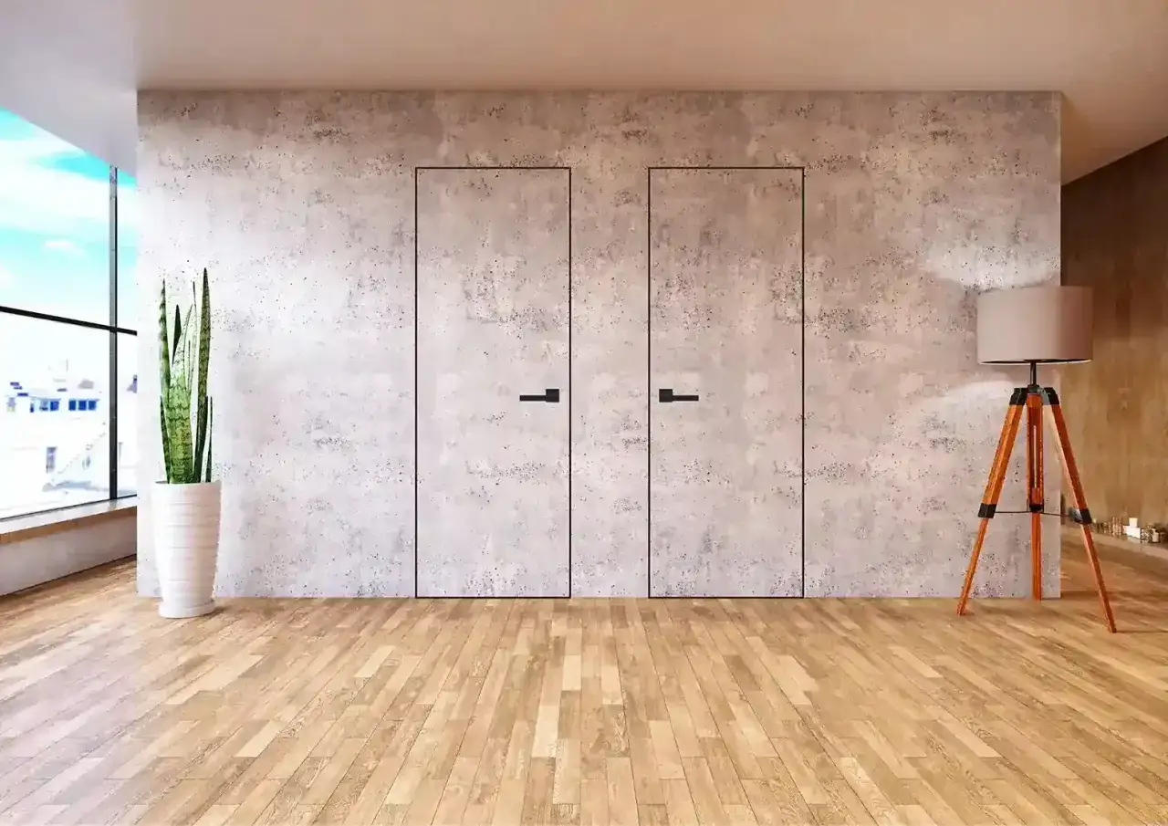 Minimalistyczne wnętrze z dwoma ukrytymi drzwiami, które idealnie wtapiają się w betonową ścianę. To sprytny sposób, jak zamaskować drzwi, tworząc gładką, jednolitą powierzchnię.