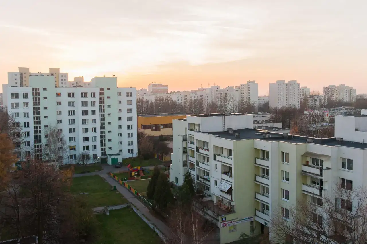 Osiedle bloków mieszkalnych o zachodzie słońca. Widać plac zabaw i zieleń. Fundusz remontowy w spółdzielni mieszkaniowej zapewnia przyszłość tym budynkom.