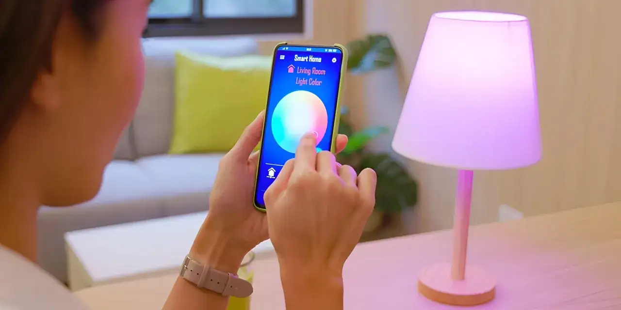 Osoba steruje oświetleniem w salonie za pomocą aplikacji smart. Wybiera kolor lampy na telefonie.