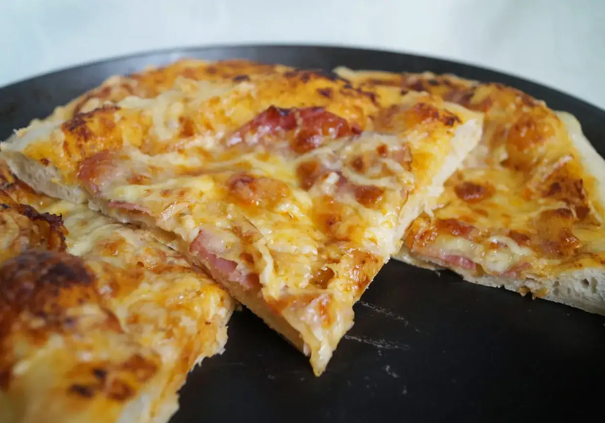 Pyszna pizza z ciągnącym się serem i kawałkami szynki, przygotowana na domowym zaczynie na pizzę.