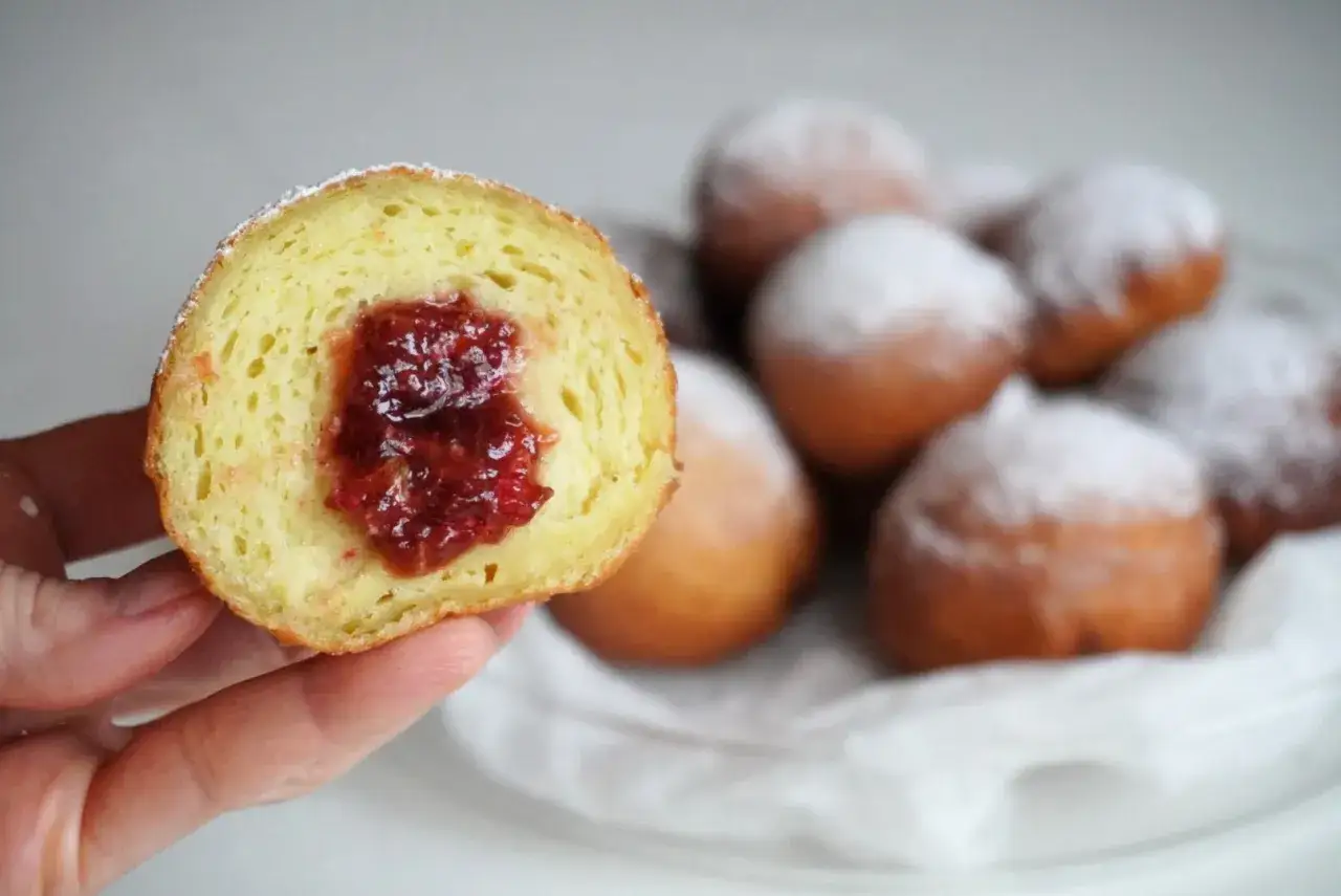 Puszyste pączki z dżemem, posypane cukrem pudrem. Czy pączki są wegańskie? Ten wygląda pysznie!