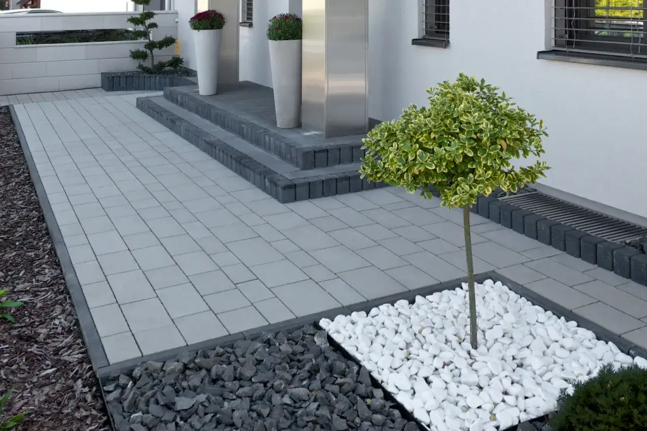 Nowoczesne **kostka brukowa inspiracje**: szary chodnik, schody z ciemnej kostki, białe kamienie i ozdobne drzewko tworzą elegancką przestrzeń.