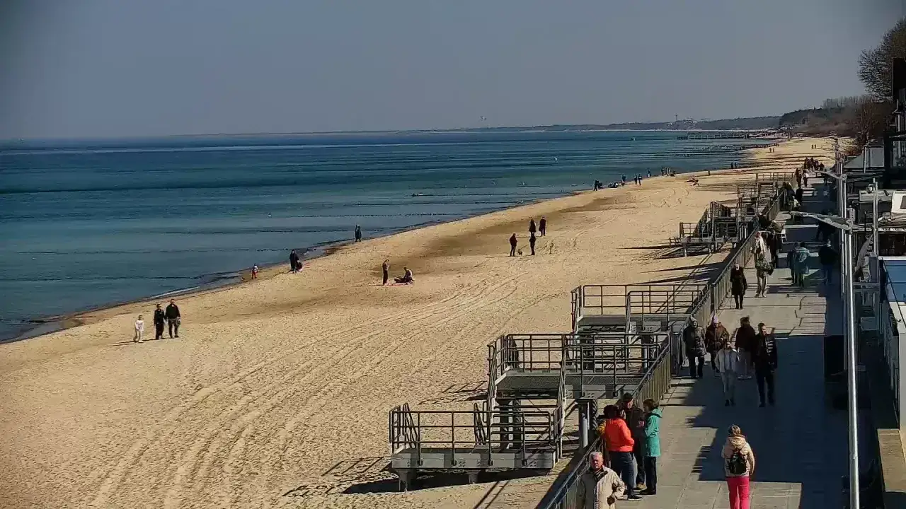 Spacer po plaży w Sarbinowie nad morzem. Ludzie spacerują po piasku i promenadzie, ciesząc się słonecznym dniem.