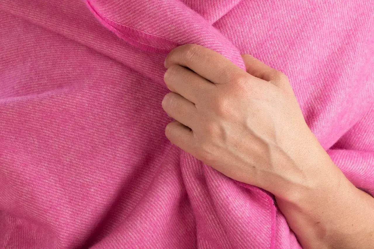 Dłoń dotyka miękkiego, r&oacute;żowego materiału. Delikatna faktura tkaniny to klucz do tego, jak rozpoznać kaszmir.