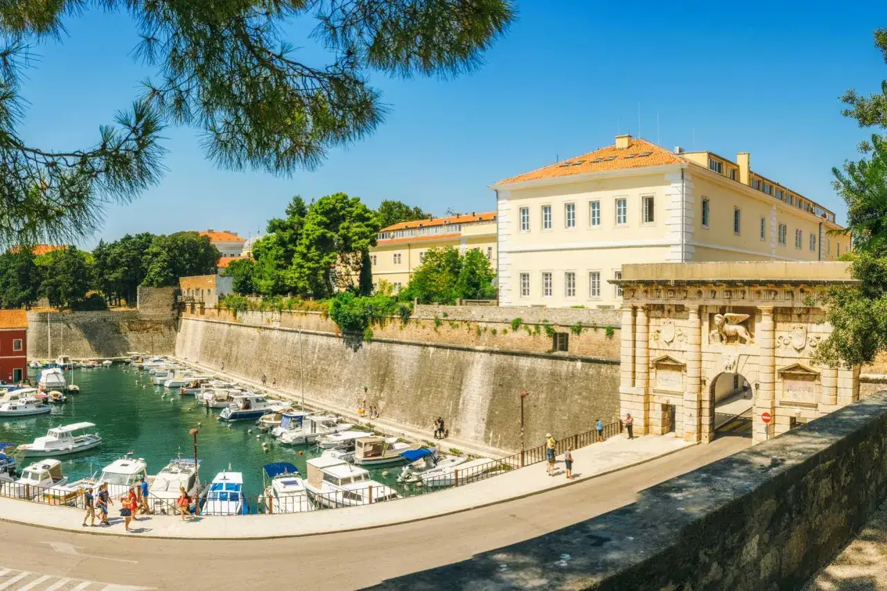 Zadar co zobaczyć: malowniczy port z łodziami, zabytkowa brama morska i kamienne mury obronne.