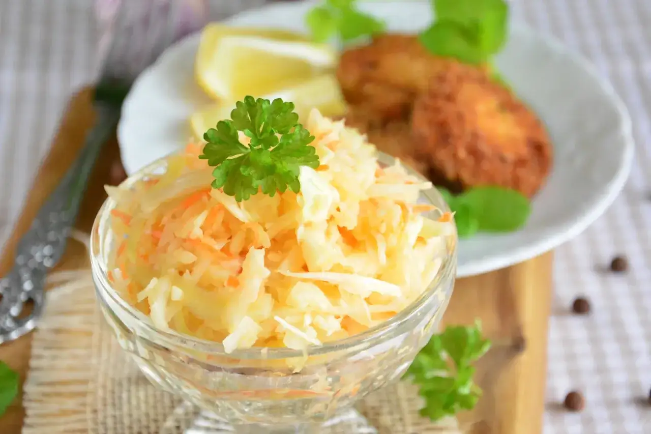 Pyszna sur&oacute;wka z kapusty i marchewki, udekorowana natką pietruszki, podana obok kotleta i cytryny.