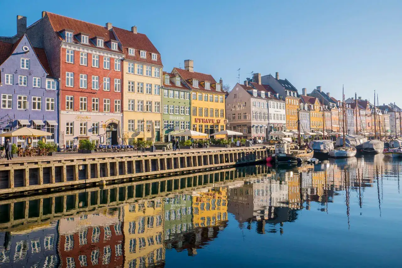 Kolorowe kamienice nad kanałem Nyhavn, idealne miejsce, by zacząć zwiedzać Kopenhagę. Łodzie i odbicia budynków w wodzie tworzą malowniczy widok.