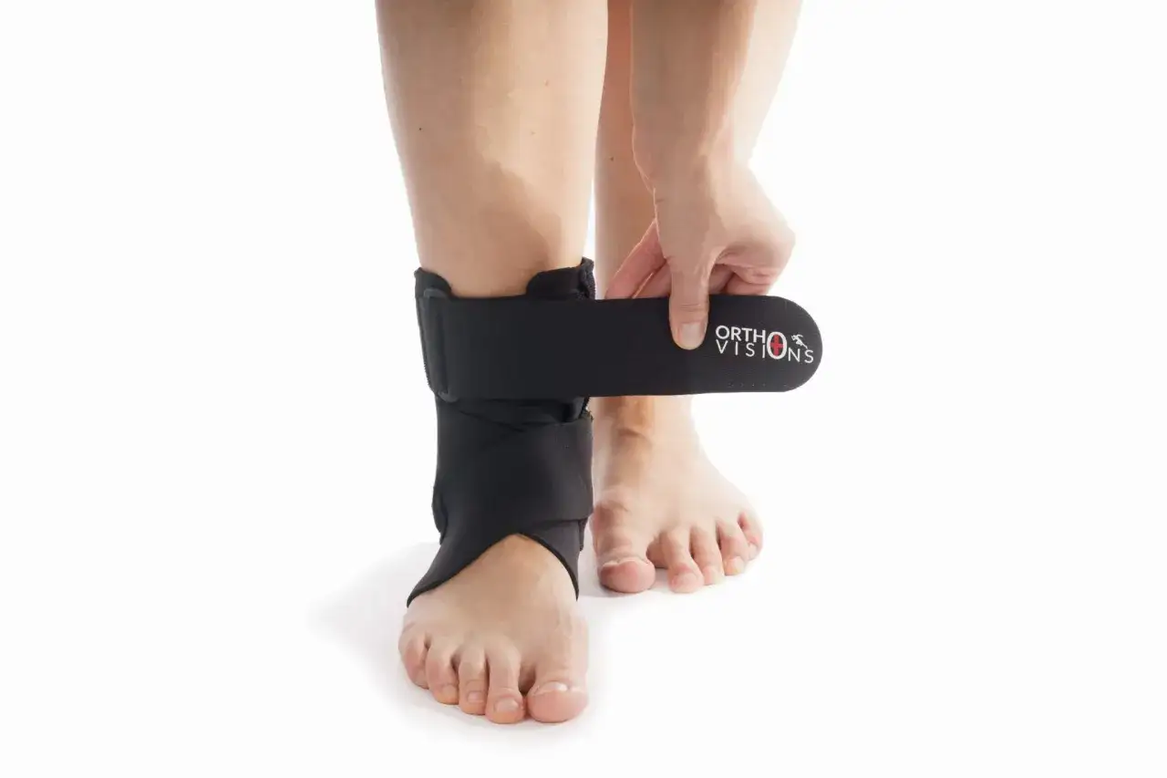 Dłoń zapina czarny ściągacz na kostkę z logo ORTHOVISIONS, zapewniając wsparcie.