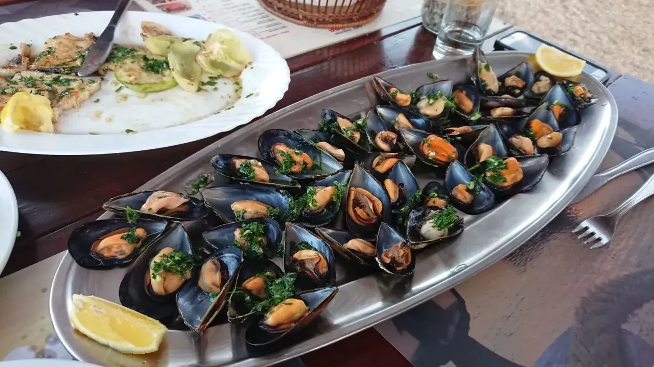 Pyszne małże z czosnkiem i pietruszką, idealne czarnog&oacute;ra jedzenie. Obok talerz z rybą i cukinią.