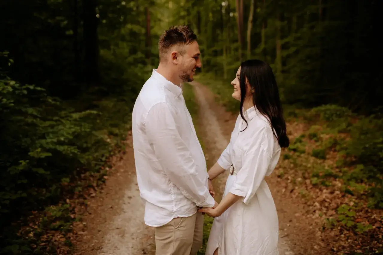 Uśmiechnięta para trzymająca się za ręce na leśnej ścieżce.