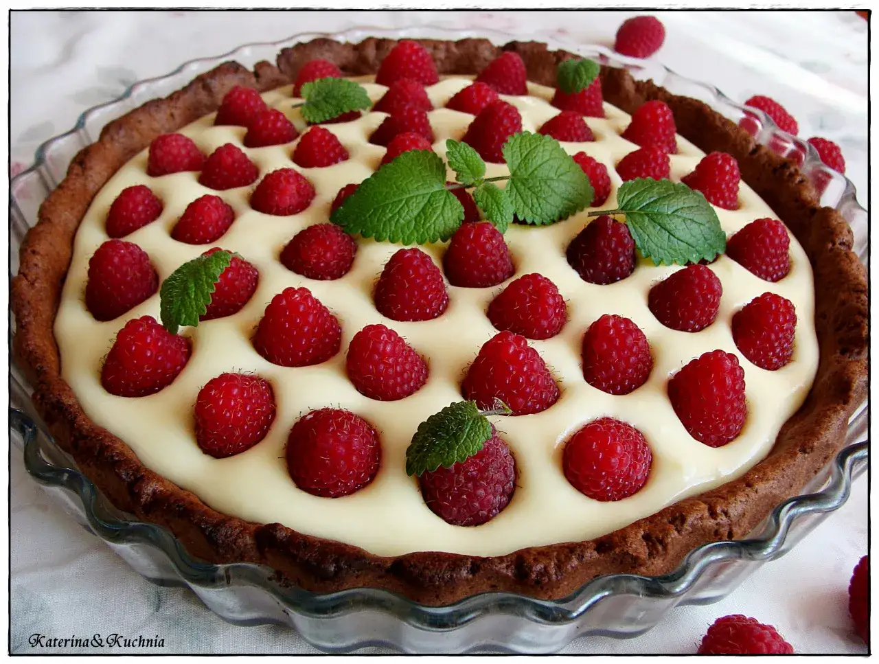 Tarta z kremem z białej czekolady, ozdobiona malinami i listkami mięty. Wygląda pysznie!