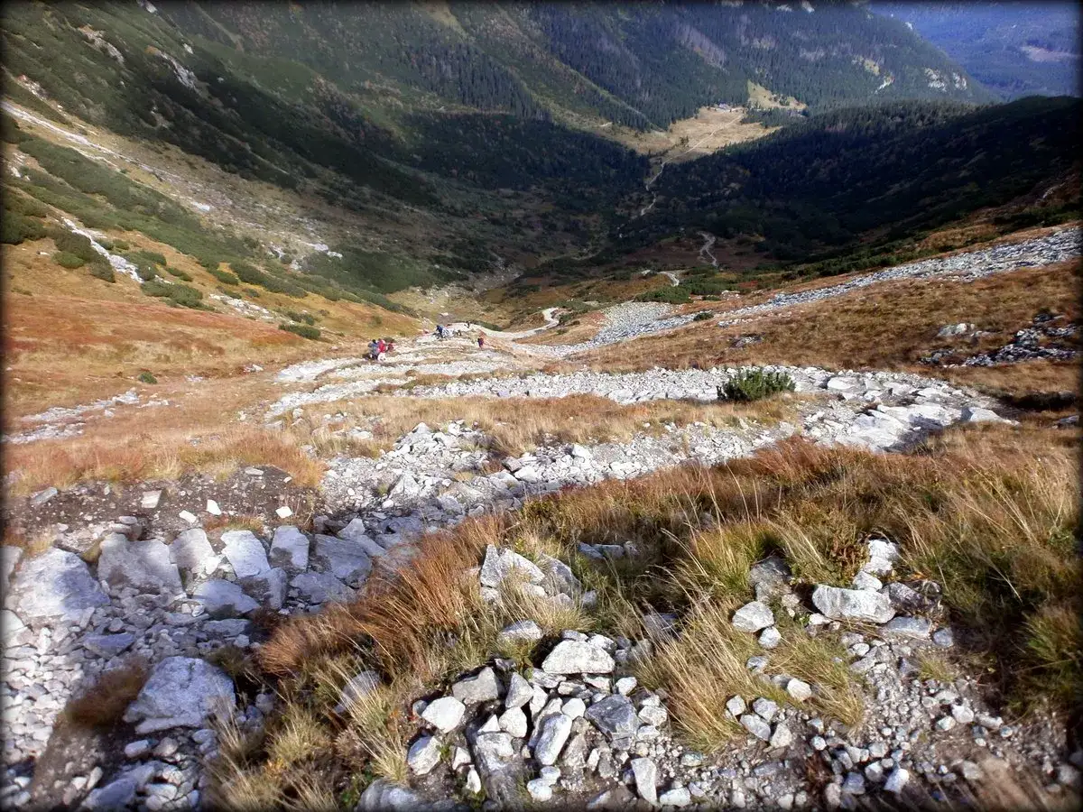 Grupa turystów schodzi kamienistym szlakiem na przełęcz pod Kopą Kondracką. Jesienne barwy gór.