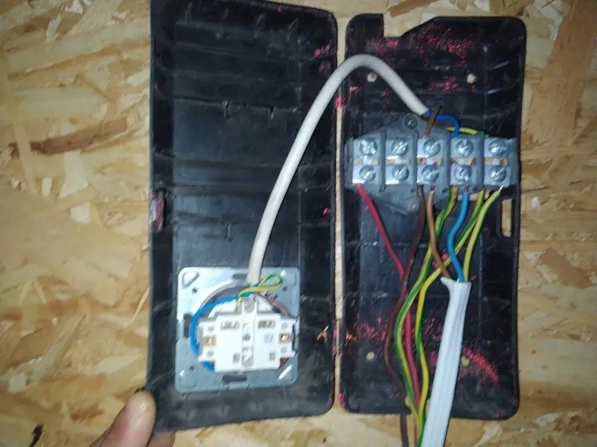 Widok na otwartą puszkę elektryczną z widocznymi, kolorowymi przewodami. Stare kolory kabli elektrycznych, takie jak brązowy, niebieski, zielono-ż&oacute;łty i czerwony, łączą się w zaciskach.